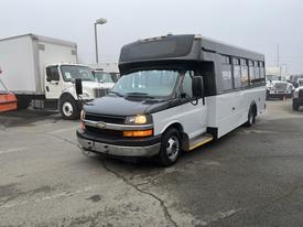 A 2017 Chevrolet Express bus with a black front and white body parked in a lot