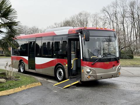 A red and gray 2016 Grande West Vicinity bus with an open door and a wheelchair ramp extended on the side
