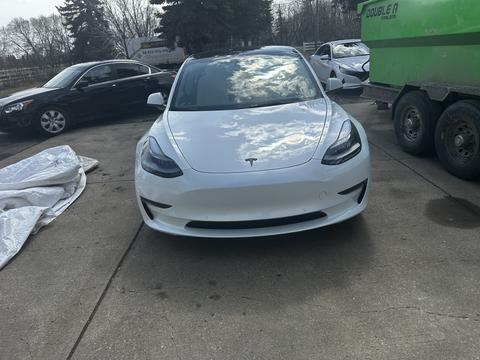 A white 2022 Tesla Model 3 is parked facing the camera with its sleek design and distinctive front grille visible