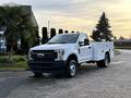 A white 2018 Ford F-350 truck with an extended cab and utility bed parked at an angle with a sturdy build and front grille prominent