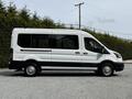 A white 2022 Ford Transit van with multiple windows and a sliding side door parked on a gravel surface