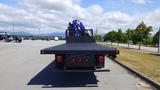 A 2017 Freightliner M2 106 flatbed truck viewed from the rear with a long black flatbed and a blue hydraulic crane mounted on the bed