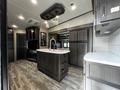 A modern kitchen interior of a 2021 Grand Design Recreational 311BHS featuring dark cabinetry an island with a sink a stove and a refrigerator