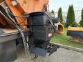 A black salt spreader mounted on the back of a 2006 Freightliner M2 106 with various hoses and a chute for distributing salt