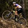 A rider on a 2025 Canyon Lux World Cup CFR AXS mountain bike ascends a rocky trail while wearing a helmet and cycling attire