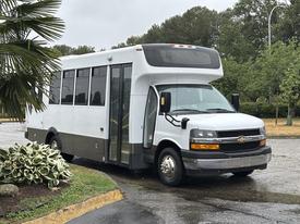 A white 2020 Chevrolet Express shuttle bus with large windows and a sliding side door parked at an angle