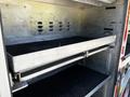 A metal shelf inside a fire truck compartment with a textured black surface and multiple ventilation holes above