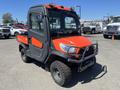 A 2014 Kubota X1100C utility vehicle with a bright orange body and black accents featuring a cab and off-road tires
