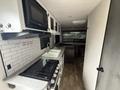 Interior view of a 2022 Keystone Hideout RDWE 20RDWE with a kitchen area featuring a stove, microwave, sink, and cabinetry along with a seating area in the background