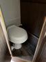 A white toilet is positioned in a small enclosed space with wooden paneling and flooring