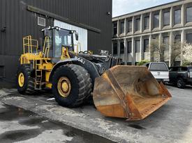 A yellow 2006 John Deere 470G wheel loader with a large bucket at the front and large tires parked beside a building
