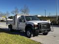 A 2008 Ford F-450 SD truck with a white exterior and a flatbed attachment parked on the side of the road