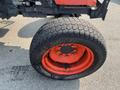 A large tire from a 2014 Kubota M7060 tractor with a rugged tread pattern and a bright orange rim