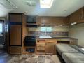 Interior of a 2014 Launch 24RLS travel trailer showcasing a kitchen area with a refrigerator oven sink and cabinetry along with a seating area and windows with natural light