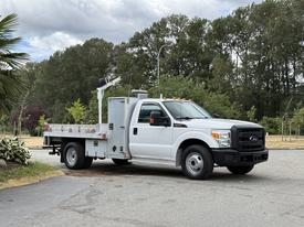 A 2015 Ford F-350 SD utility truck with a flatbed and a mounted tool rack on the side