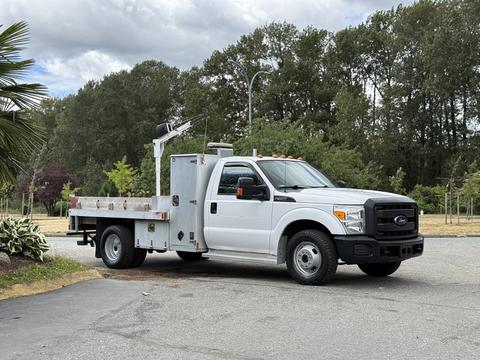 A 2015 Ford F-350 SD utility truck with a flatbed and a mounted tool rack on the side