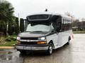 A 2019 Chevrolet Express bus with a black front and white body parked on a wet surface