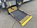 A foldable wheelchair ramp with a yellow edge deployed from the back of a vehicle designed for accessibility