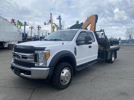 White 2017 Ford F-550 with a flatbed and attached crane in the foreground