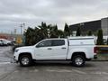 A white 2019 Chevrolet Colorado pickup truck parked with a utility cap on the bed and chrome wheels