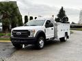 A 2017 Ford F-550 in white with a utility bed and equipment mounted in the back parked on a driveway