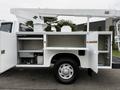 A 2001 Ford F-350 with a white exterior featuring an elevated bucket truck mechanism and multiple open compartments on the side for tools and equipment