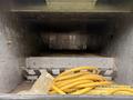 A metal storage compartment with a flat metal base and a set of raised teeth at the edge contains a coiled yellow power cord on the bottom