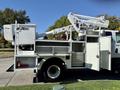 A 2010 International 4300 utility truck with an Altec aerial lift, featuring an open service compartment and a raised boom arm for accessing elevated areas