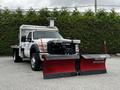 A 2011 Ford F-550 plow truck is positioned with two large red snow plows mounted at the front and a metal utility bed at the rear