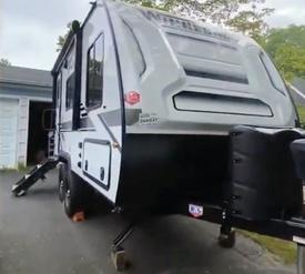 A 2020 Winnebago MICRO MINI travel trailer with a sleek design featuring a white exterior and a compact layout, positioned on a set of stabilizing legs