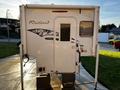 A white 2023 Westland 80W 8 Foot camper with a door and window on one side, featuring a sleek design and mounted on a set of leveling blocks