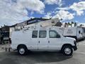 A white 2008 Ford Econoline van with a ladder rack and bucket lift attached on the roof
