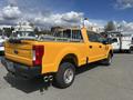 A yellow 2017 Ford F-250 Super Duty truck with a silver metal ladder rack and dual exhaust pipes is parked in a lot