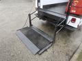 A loading ramp is extended from the back of a 2000 Ford F-450 truck with a textured surface and chain supports