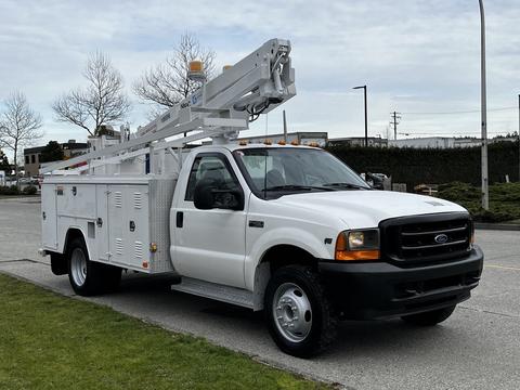 A white 2001 Ford F-450 Super Duty truck with a bucket lift attached and tool storage compartments on the sides