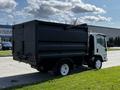 A 2016 Isuzu NPR with a black dump bed and white wheels parked on grass
