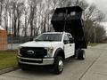 A white 2019 Ford F-550 truck with a raised dump bed showcasing its large front grille and chrome accents