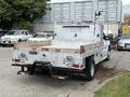 A white 2015 Ford F-350 SD with a flatbed and tool compartments is parked, showcasing its utility design and rear-mounted work lights