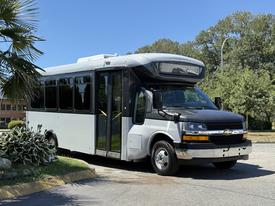 A 2019 Chevrolet Express bus with a black front and silver body featuring large windows and a passenger entrance door on the side