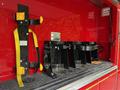 A set of black metal brackets with yellow straps mounted inside a red vehicle compartment designed for securing equipment or tools