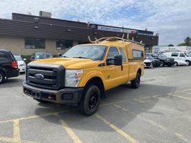 A yellow 2013 Ford F-250 SD pickup truck with a utility cap and roof racks parked in a lot