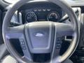 Steering wheel of a 2012 Ford F-150 with buttons and controls visible along with the instrument cluster displaying speed and fuel gauge
