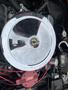 A shiny chrome air cleaner with a central opening sits atop a vintage Chevrolet Corvette engine featuring red wires and various engine components