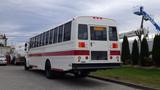 A white 2013 Freightliner M2 106 bus with a red stripe along the side and multiple windows is parked with its rear facing the viewer