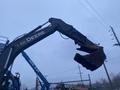 A 2014 John Deere 350G excavator arm with a bucket attachment raised high against a cloudy sky