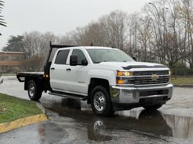 A 2015 Chevrolet Silverado white pickup truck with a flatbed in the foreground standing on a wet surface