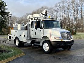 A 2013 International Durastar 4300 utility truck with a white exterior featuring a boom lift apparatus and storage compartments on the side