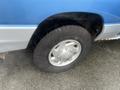 A blue and silver 2006 Ford Econoline van with a close-up view of its right front tire and wheel rim