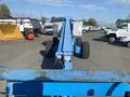 A blue 1997 Genie S-65 4X4 lift with large wheels and extended boom positioned forward in a parking lot