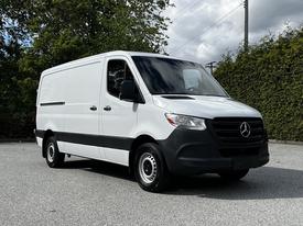 A white 2020 Mercedes-Benz Sprinter van with a sleek design and black accents in the front, featuring large windows and sturdy wheels